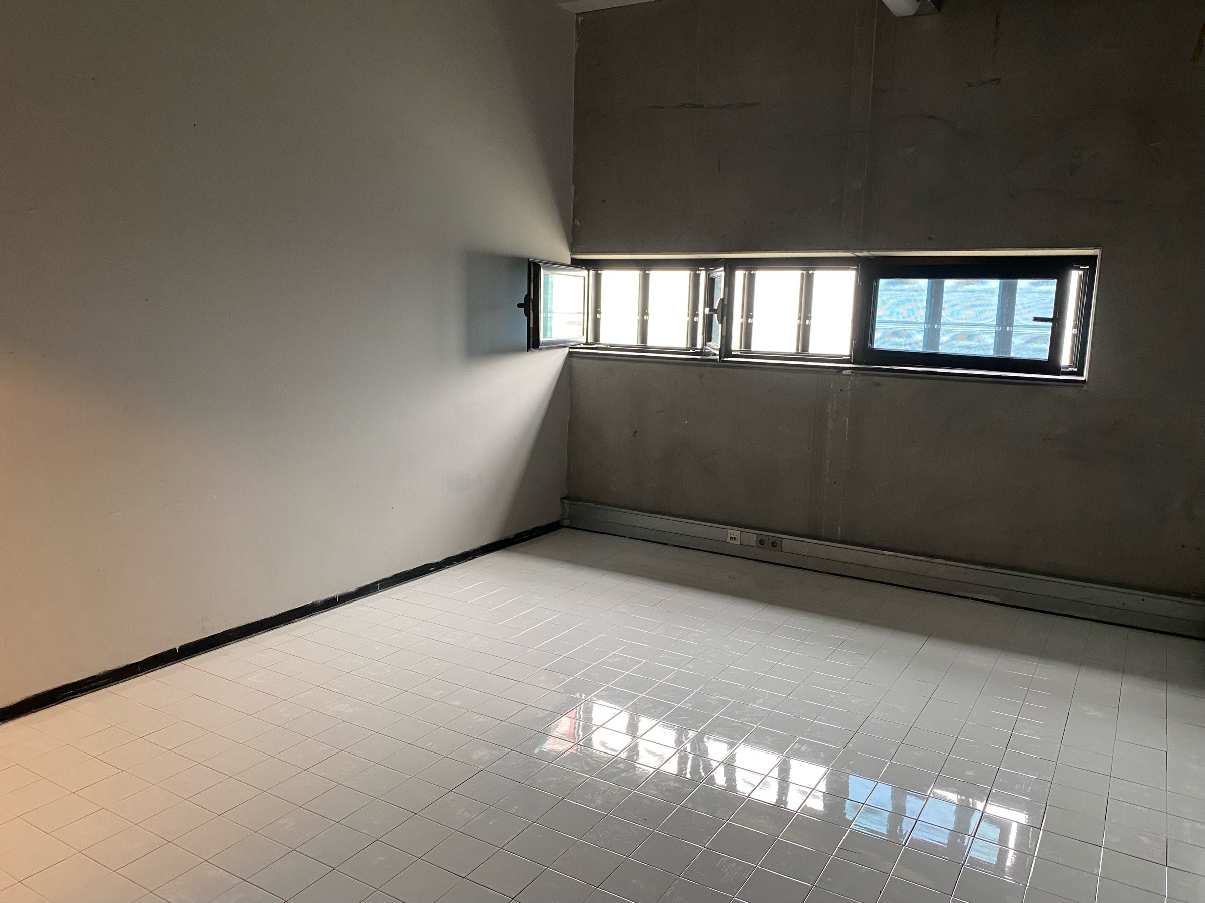 An empty concrete room with a glossy white tiled floor and a row of high windows.